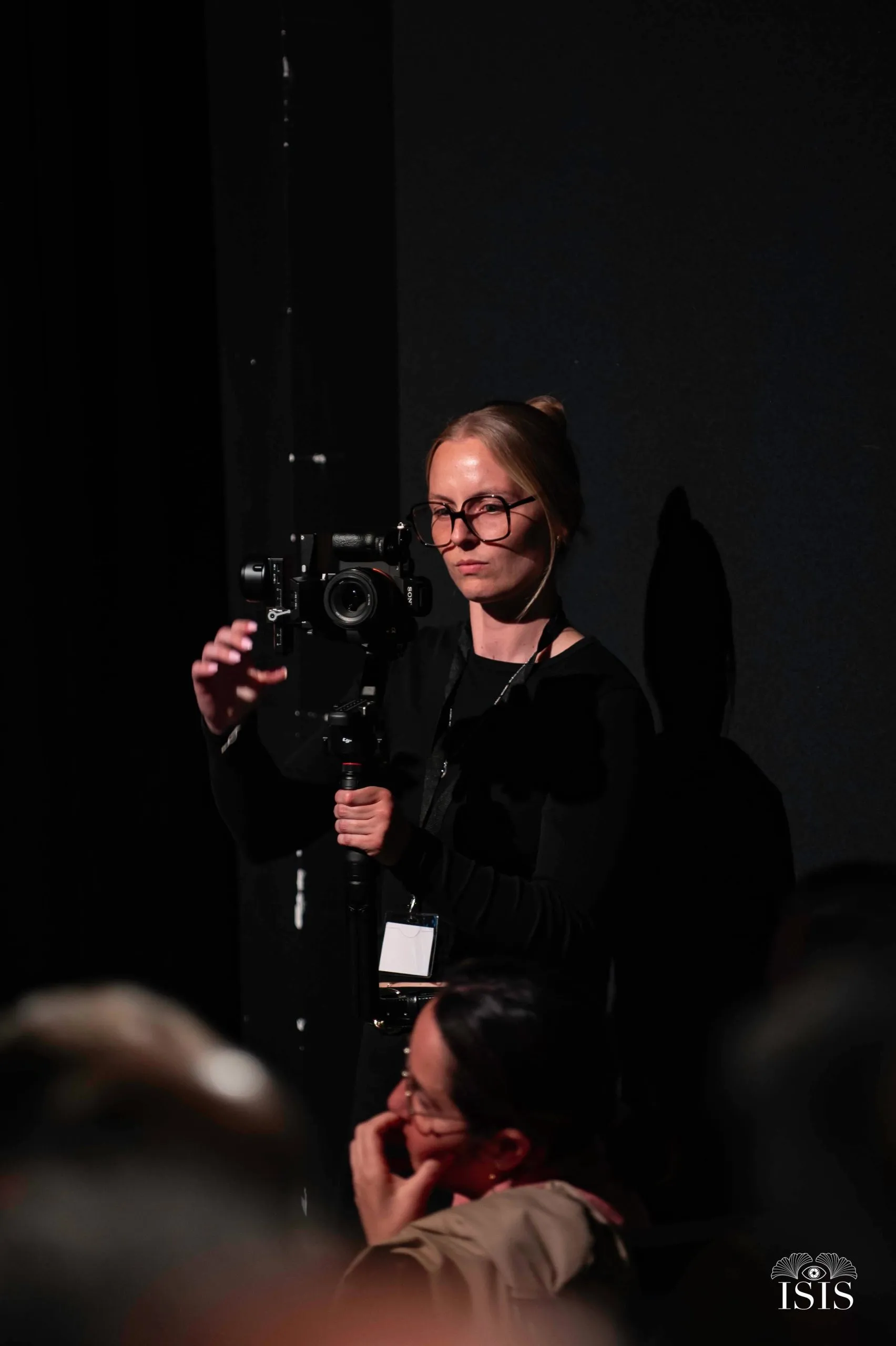 Océane Chesnais filme une conférence dans une salle sombre, badge autour du cou, caméra au stabilisateur