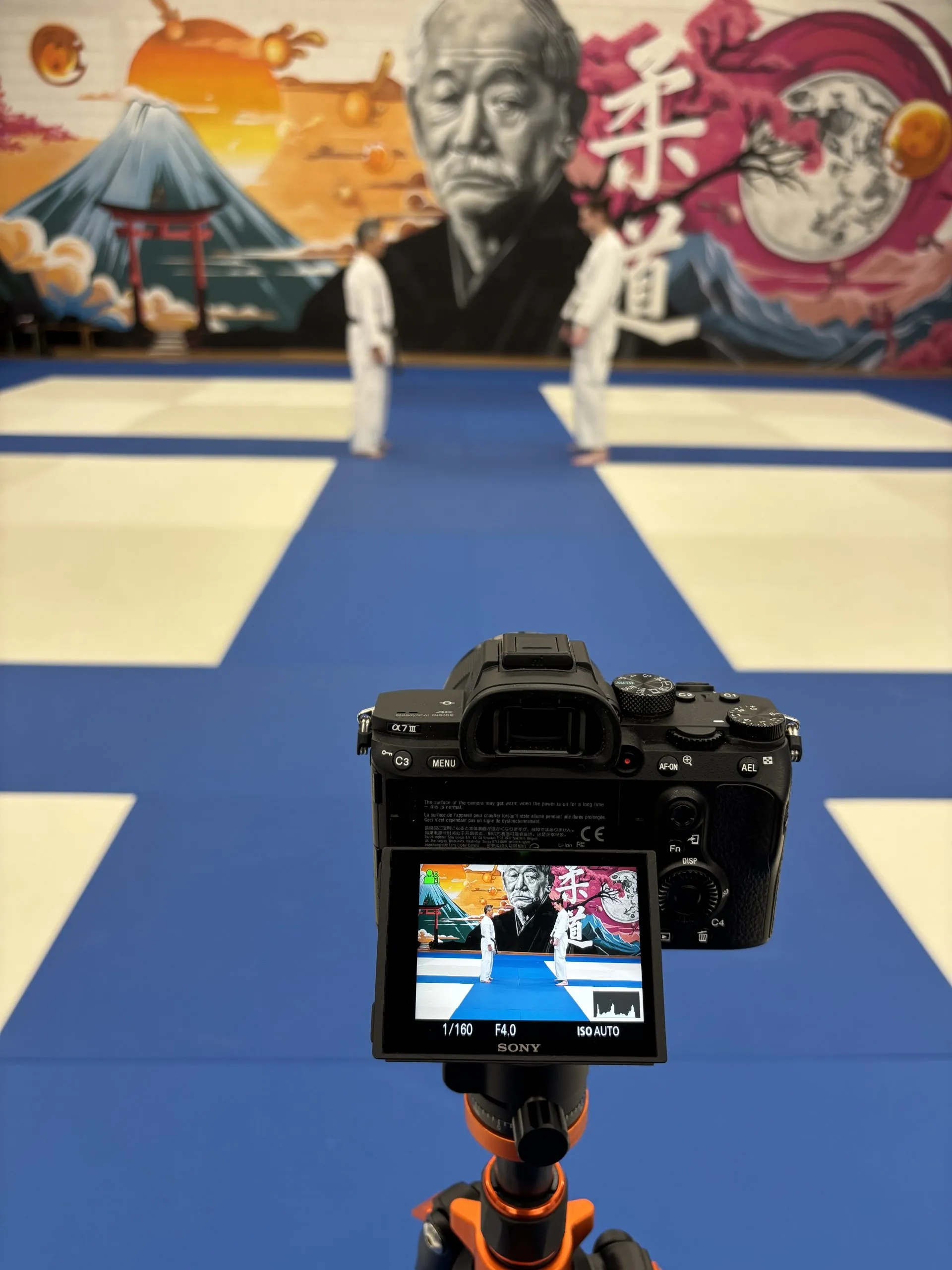 Caméra Sony sur trépied face à deux judokas dans un dojo de Chartres décoré d’une fresque