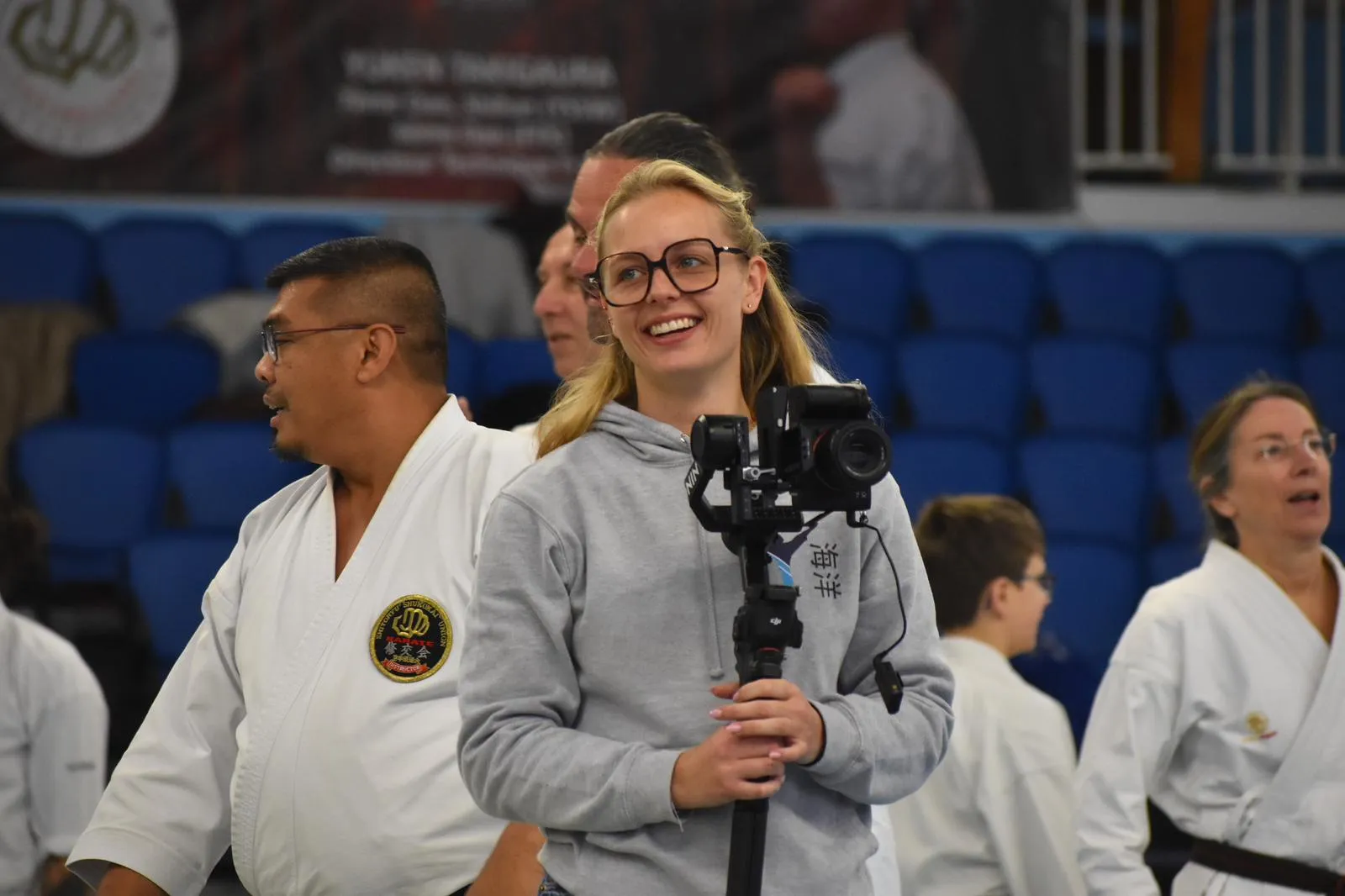 Océane Chesnais souriante, caméra au stabilisateur, entourée de karatékas